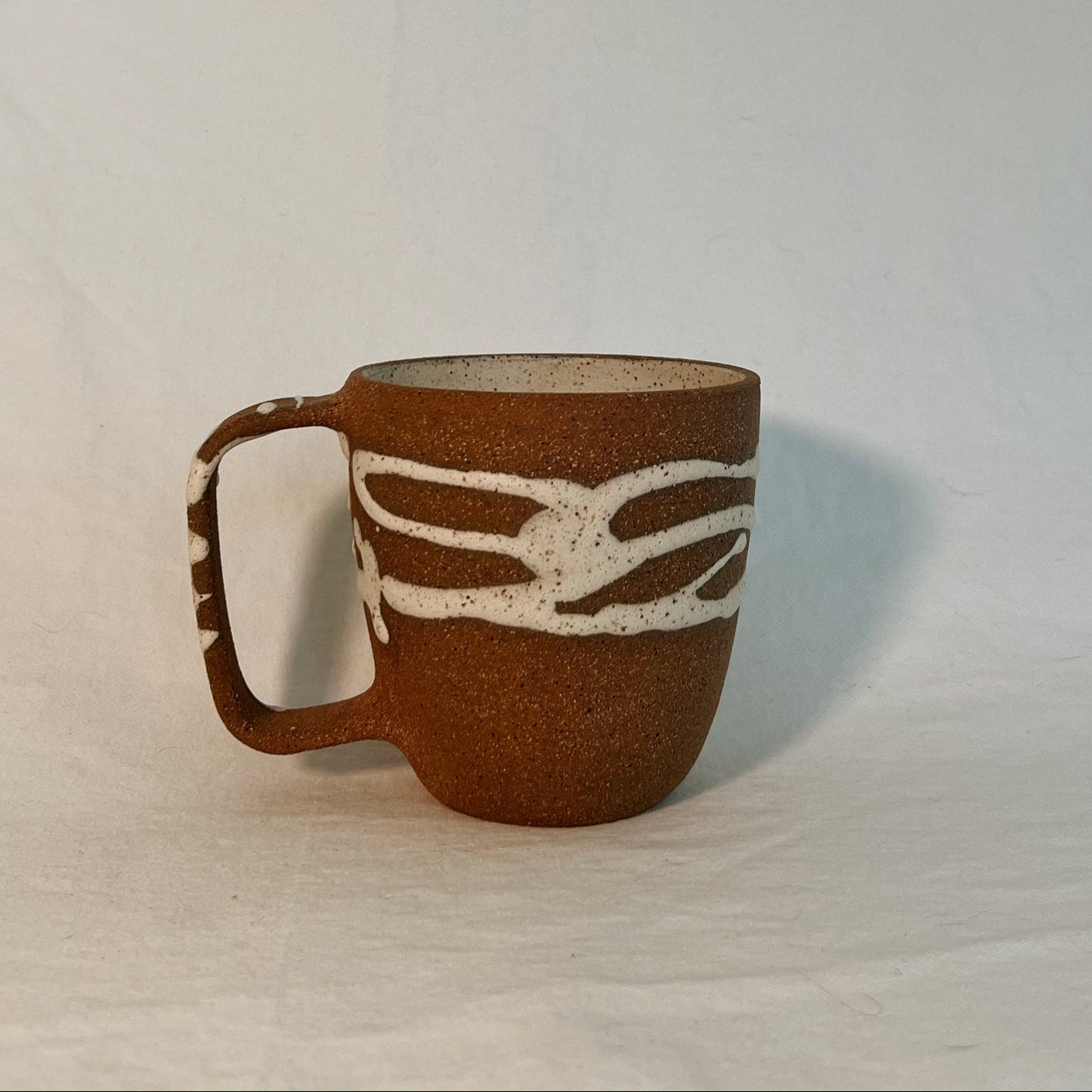 Brown ceramic mug with handle, with white drizzled glaze design on a white background